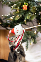 Cat playing with a snowman toy in front of a decorated Christmas tree.