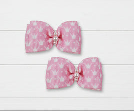 Two pink canine hair bow clips with white heart patterns and pearl centers on a white background