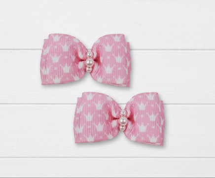 Two pink canine hair bow clips with white heart patterns and pearl centers on a white background