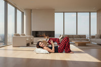 Woman in red and black plaid pajama pants lying on a white surface with a dog wearing a matching outfit.