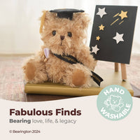 Graduation-themed teddy bear with a cap and diploma, sitting on a table with a 'Hand Washable' label.