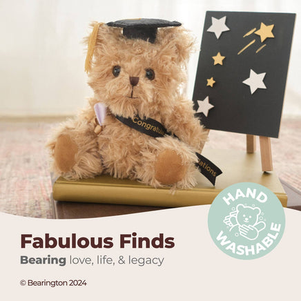 Graduation-themed teddy bear with a cap and diploma, sitting on a table with a 'Hand Washable' label.