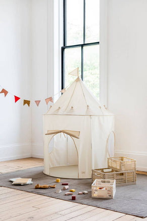 Children's play area with a white play tent, toys, and a small table in a room with large windows.