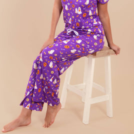 Person wearing purple Halloween-themed pajamas sitting on a white stool against a beige background