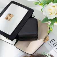 Black jewelry case with mirror on a white surface with flowers
