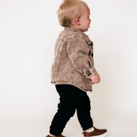 Child wearing a denim jacket and black pants on a plain background