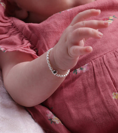 Baby's hand wearing a pearl bracelet on a pink fabric background