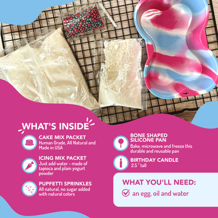 Cake making kit with cake mix packets, silicone pan, birthday candle, and sprinkles on a wooden surface.