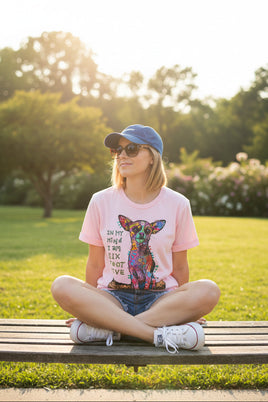 Pink t-shirt with colorful dog graphic and text, paired with denim shorts and white sneakers on a wooden surface.