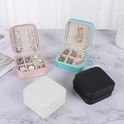 Four jewelry cases in different colors with jewelry inside on a marble surface.
