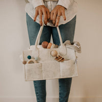 Person holding a beige bag with wooden toys against a neutral background