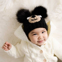 Child wearing a black knit hat with fluffy ears on a white background