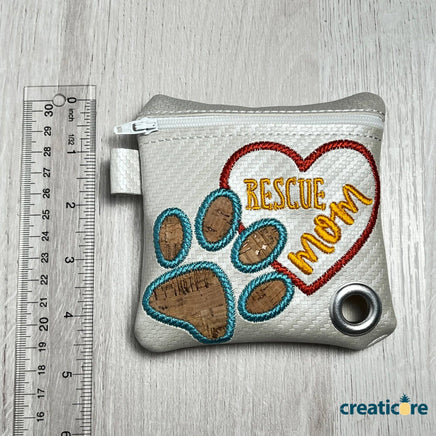 handmade poop bag dispenser with clip in white. embroidered wording that says rescue mom with a cute little cork shaped paw on the front. comes with a fee bag of poop bags. 