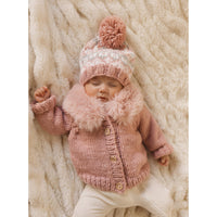 Baby in a pink knitted outfit with a matching hat on a soft beige blanket