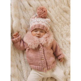 Baby in a pink knitted outfit with a matching hat on a soft beige blanket
