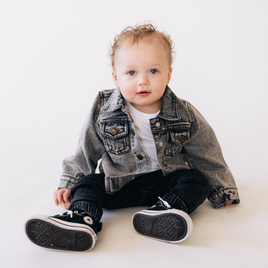 Baby wearing a denim jacket and black sneakers on a white background