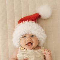 Baby wearing a knitted Santa hat against a beige background
