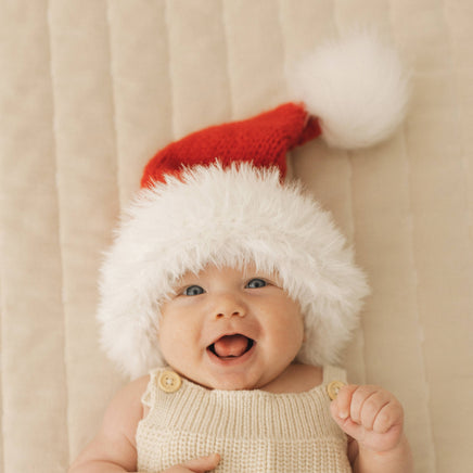 Baby wearing a knitted Santa hat against a beige background