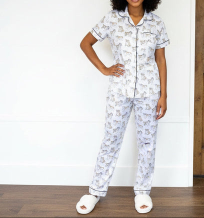 Woman wearing a white pajama set with dog pattern in front of a wooden door.