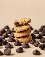 Stack of chocolate chip cookies surrounded by chocolate chips on a beige background