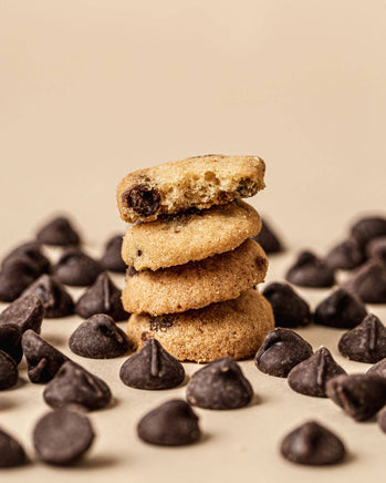 Stack of chocolate chip cookies surrounded by chocolate chips on a beige background