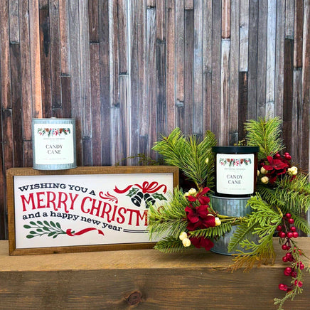 Christmas-themed decor with candles and a sign on a wooden surface against a wooden wall.