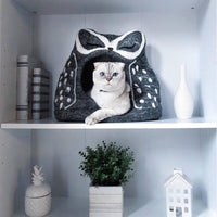 Cat peeking out from a gray pet house with white polka dots on a shelf.