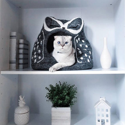 Cat peeking out from a gray pet house with white polka dots on a shelf.
