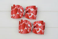 Two red and white heart-patterned dog bows with silver centers on a white background