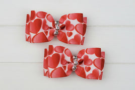 Two red and white heart-patterned dog bows with silver centers on a white background