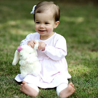 Child in a white dress holding a stuffed animal on grass