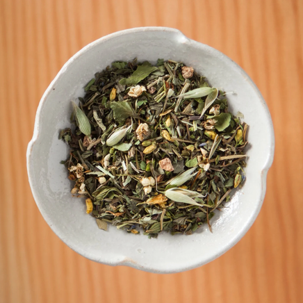 White bowl filled with green herbal tea leaves on a textured orange background