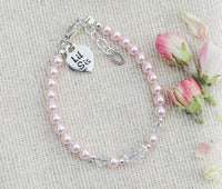 Pink pearl bracelet with sterling silver charms that say Lil Sis on a beige fabric background