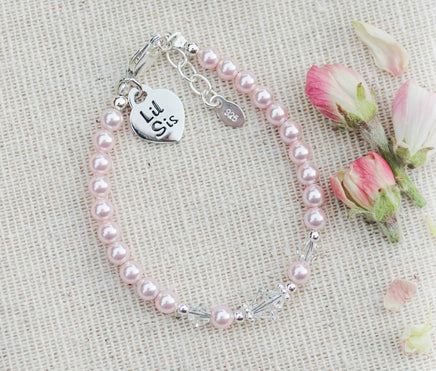 Pink pearl bracelet with sterling silver charms that say Lil Sis on a beige fabric background