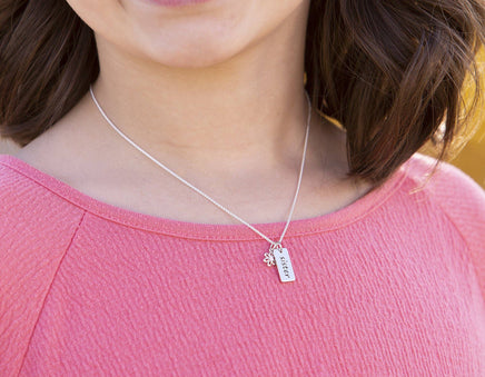 girl wearing a sterling silver sister necklace with two charms on a pink shirt