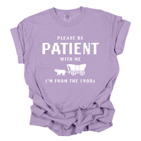 Purple t-shirt with white text and graphic on a white background. the t shirt says please be patient with me I'm from the 1900s 
