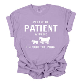 Purple t-shirt with white text and graphic on a white background. the t shirt says please be patient with me I'm from the 1900s 