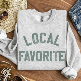 Gray sweatshirt with 'LOCAL FAVORITE' text on a white surface with casual items around