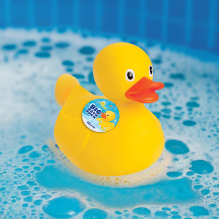 A large yellow rubber ducky floating in a bathtub filled with bubbles, with a bright blue label on its back.
