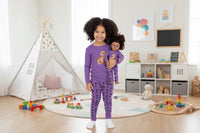 Child wearing purple pajamas with a matching doll on a white background
