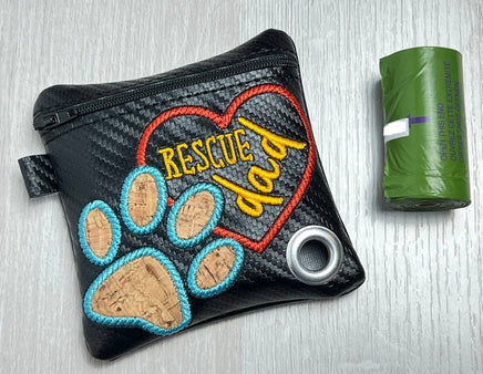 Black pouch with embroidered 'Rescue Dad' text and paw prints next to a green trash bag on a light gray background